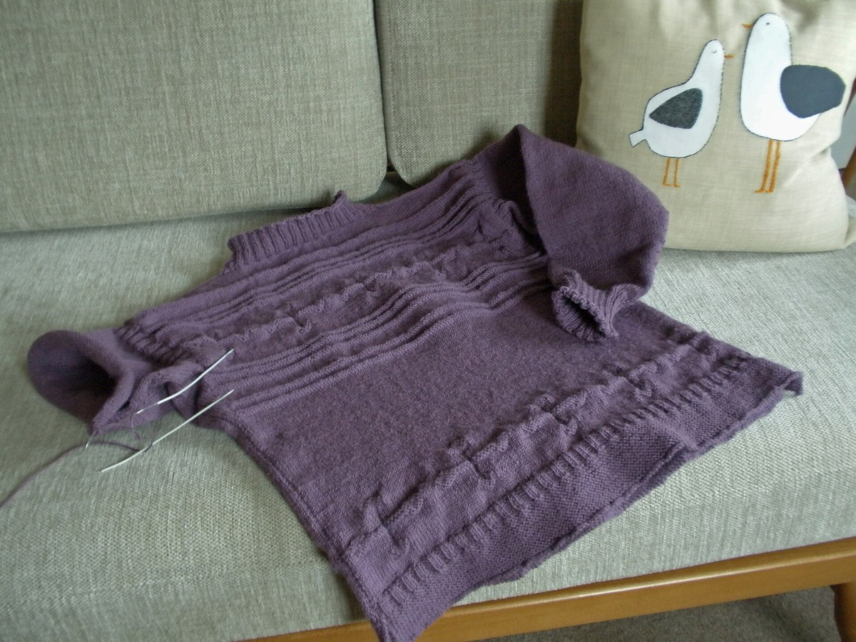 A hand-knitted gansey sweater in progress, with the knitted fabric and working yarn visible